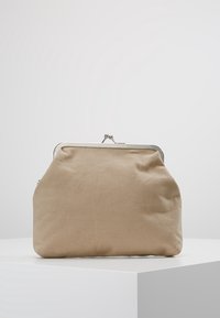 Beige stof møntenpung med sølvmetalspænde, der hviler på en hvid overflade mod en ensartet lysegrå baggrund.