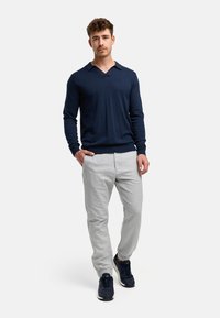 Suéter de punto azul marino con escote en V y mangas largas, combinado con pantalones tapered de color gris claro y zapatillas oscuras, creando un conjunto casual.