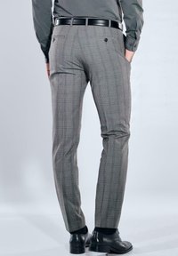 Graue karierte Hose mit schmaler Passform, ausgestattet mit zwei Gesäßtaschen und einem schwarzen Ledergürtel. Kombiniert mit schwarzen Lederschuhen.