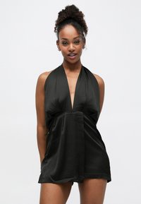 Schwarzer Satin-Jumpsuit mit Neckholder, tiefem V-Ausschnitt, legerer Passform und fließenden Shorts. Glatte Textur und minimalistisches Design.