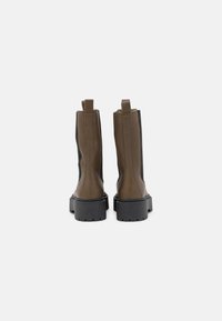 Bottines en cuir marron avec des panneaux latéraux noirs, bout rond, forme épurée, languettes de tirage et semelles en caoutchouc noir épaisses.