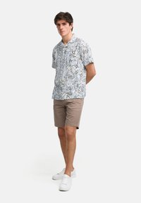 Kortermet, lyseblå skjorte med blomstermønster og svarte detaljer, kombinert med beige shorts og hvite joggesko.