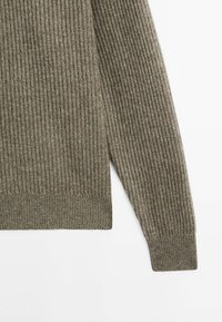 Geribd breiselsweater in olijfgroen, met lange mouwen en een aansluitende zoom. De textuur is zacht met een subtiel patroon door het hele kledingstuk.