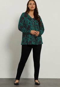 Donkergroene blouse met een bladmuster, lange mouwen, v-hals en knoopdetails. Gecombineerd met zwarte slim-fit broeken en zwarte ballerina's.