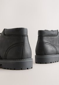 Schwarze knöchelhohe Lederstiefel mit glatter Textur, kontrastierenden Nähten und strukturierten Gummisohlen mit tiefem Profil für besseren Halt.