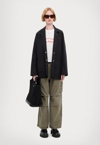 Musthave must kõva jakki, valge t-särk punase tekstiga, khaki värvi cargo-püksid, must tekstuuriga kott, paksud mustad kingad, sirged blondid juuksed.