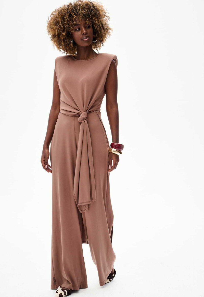 Maxi-jurk van zacht, gedempt bruin materiaal met een asymmetrische knoopdetail bij de taille en zijspleten, met gestructureerde schouders en een gladde textuur.