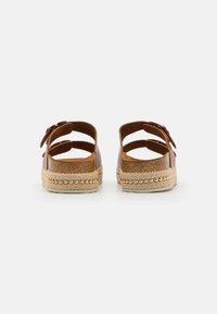 Sandalias de cuero marrón con dos correas ajustables, plantilla de corcho, suela trenzada de yute y acentos de cuentas doradas a lo largo del borde.