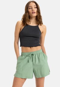 Zwarte geribbelde crop top met een geschulpte zoom, gecombineerd met losvallende, lichtgroene shorts met een elastische tailleband en zijzakken.
