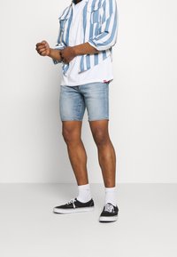 Světle modré denimové šortky, bílé tričko a dlouhý modro pruhovaný svetr; černé tenisky s bílou podrážkou a bílé ponožky do kotníků.