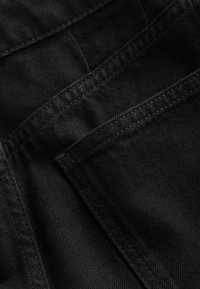 Fekete farmer anyag, sima textúrával, varrási részletekkel és két félig látható zsebbel, amelyek átlapolva helyezkednek el.