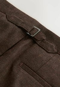 Tissu en mélange de laine marron avec un motif en chevron, comportant une fermeture à boucle sur le côté, une texture lisse et des coutures d'accent sur les poches.