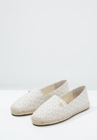 Espadrilles blancas con un patrón geométrico, suela de yute, y un pequeño logo en el lateral. Textura de lona suave.