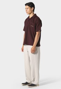 Polo a maniche corte color bordeaux con taschino, tessuto testurizzato, dettaglio logo discreto, abbinato a pantaloni a gamba larga color crema e scarpe nere.