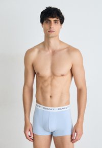 Helles blaues Boxershorts mit einem weißen Bündchen, das das wiederholte Logo "GANT" zeigt. Der Stoff wirkt glatt und eng anliegend.