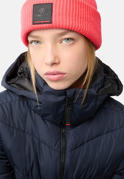 Marineblaue Steppjacke mit hohem Kragen und diagonalen Nähten, kombiniert mit einer leuchtend pinken Rippstrickmütze mit einem Logo-Patch.