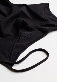 Bañador de tela negra con textura suave, tirantes finos y una etiqueta con instrucciones de cuidado visible en el interior.