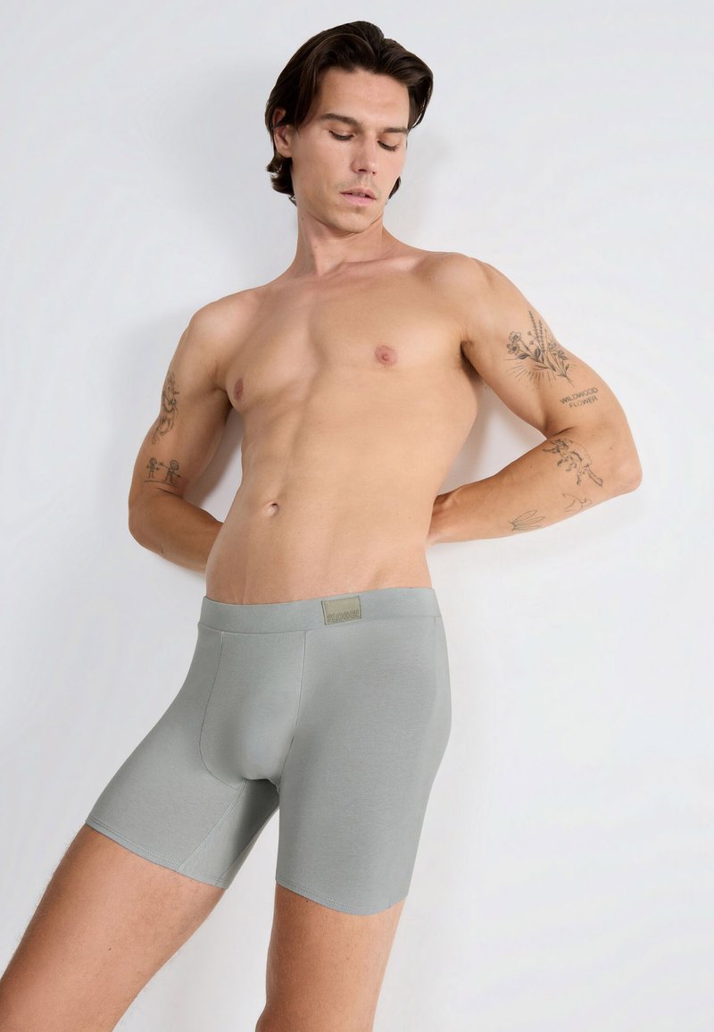 Hellgraue Boxershorts aus glattem Stoff, mit einem weichen Bündchen und einem Logo-Tag, in einer körperbetonten Passform, die die Silhouette betont.