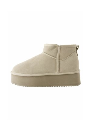 Botte de cheville en daim beige avec un bout rond et une épaisse semelle plateforme. Présente un tirant et des détails de couture le long des coutures.