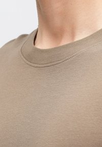 Lässig beiges T-Shirt mit Rundhalsausschnitt, kurzen Ärmeln und einer weichen, glatten Textur. Nahtdetails rund um den Hals.