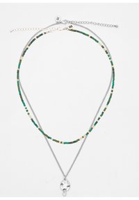 Meerdere strengen ketting met een zilveren ketting en edelsteenparels in groen en room, met een ronde hanger die bloemenpatronen toont.
