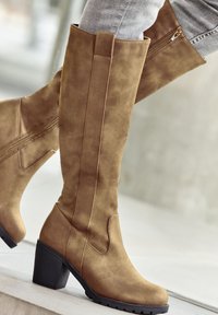 Knee-high brown faux suede boots with a block heel, featuring a zipper on the side and a smooth texture, ideal for casual wear.