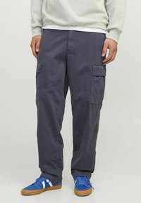 Mørkegrå cargo bukser med store sidelommer, lige ben-design og en slidstærk stofstruktur. Matchet med blå sneakers med hvide accenter.