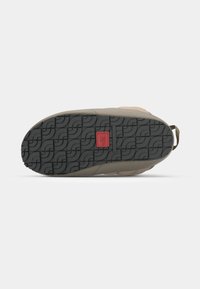 Semelle en caoutchouc noir texturé avec un motif de semelle ondulée, présentant une accent rouge et une partie supérieure beige intégrée harmonieusement.