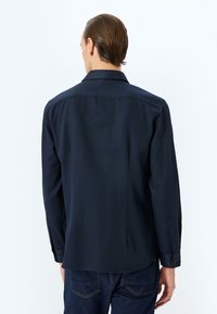 Mörkblå långärmad skjorta, knappdown-krage, rak skärning, slät textur, rundad fåll, med synlig sömnad och knapprader vid ärmarna.