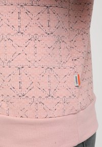 Sweatshirt rose clair avec un motif géométrique en rose plus foncé et noir. Poignets et ourlet côtelés, avec une petite étiquette de marque sur le côté.