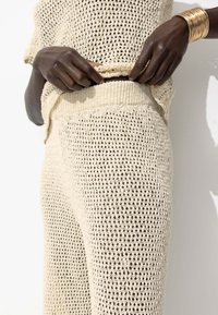 Ensemble en tricot deux pièces de couleur beige clair, avec une texture à mailles ouvertes. Le haut a une coupe ample et le bas est doté d'une taille côtelée.
