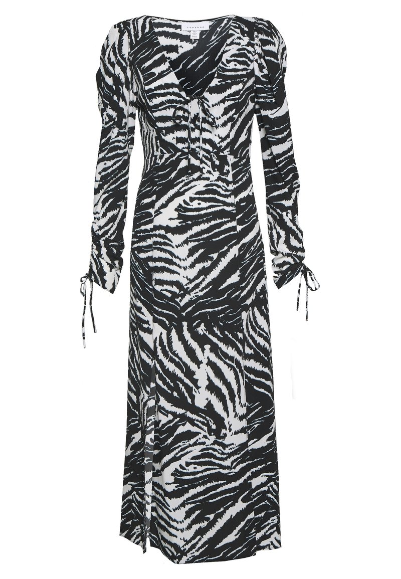 Randig klänning i svart och vitt med zebramönster, långa ärmar med knyt detaljer, v-ringning, flödande siluett och slits på sidan för extra rörelse.