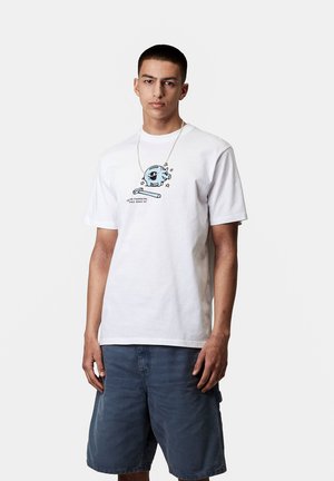 Camiseta blanca de algodón con un gráfico de una hucha azul y estrellas. Cuello redondo, mangas cortas, corte relajado. Lleva puesta con pantalones cortos azules.