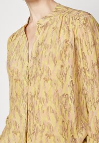 Blouse in lightweight fabric featuring a pink and yellow abstract pattern with textured detailing and a mandarin collar. Buttons down the front.