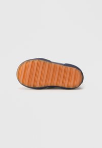 Sole di scarpa con un motivo rigato in gomma arancione, incorniciata da un materiale blu navy scuro, con una texture liscia per migliorare la presa.