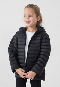 Giacca a vento nera con design trapuntato orizzontale, cappuccio attaccato, cerniera frontale e fodera blu a contrasto. Indossata sopra una camicia bianca.