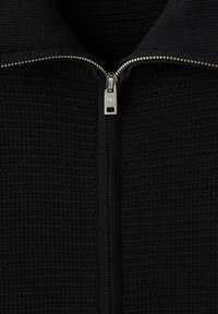 Czarna dzianinowa kurtka na zamek z srebrnym suwakiem, teksturowaną tkaniną i wysokim kołnierzem. Szwy są mocno zszyte dla trwałości.