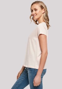 T-shirt en coton rose clair à manches courtes, coupe décontractée, col rond et détails de couture subtils, associé à un jean bleu.