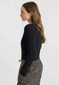 Pull en maille côtelée noire à manches longues associé à un pantalon à imprimé léopard avec cordon de serrage, offrant une coupe décontractée et des poches latérales.