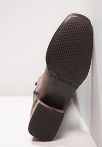 Braune Wildleder-Ankle-Boots mit niedrigem Absatz, strukturiertem Gummisohle, seitlichem Reißverschluss und abgerundeter Zehenpartie. Mit Logo-Prägung an der Ferse.