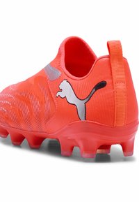 Botas de fútbol naranja brillante con suela con tacos, lengüeta en el talón y un prominente logo de Puma en blanco y negro en el lateral.