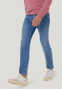 Blaue Denim-Jeans mit geradem Schnitt, kombiniert mit weißen und beigen Sneakers. Einfaches Design, mittlere Waschung, keine sichtbaren Abnutzungen.