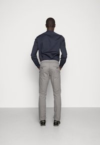Šedé slim-fit kalhoty s kapsami vzadu a námořnickou košilí s dlouhým rukávem. Boty jsou černé s světlou podrážkou. Minimalistický design, jednobarevné.