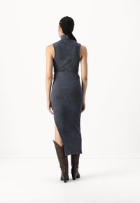 Σκούρος γκρι ριπ με ύφανση φόρεμα με ψηλό γιακά, εφαρμοστή σιλουέτα, πλαϊνό άνοιγμα και συνδυασμένο με καφέ καουμπόικες μπότες. Λείο υλικό, μήκος μέχρι τις γάμπες.