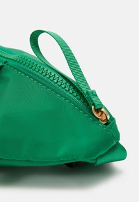 Borsa in nylon verde con forma diagonale, caratterizzata da una cerniera dorata e un anello di tessuto per una facile impugnatura. Texture liscia e cuciture dettagliate.