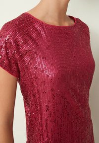 Top rojo con lentejuelas, que presenta un escote redondo y mangas cortas, con una textura de rayas verticales que realza su calidad reflectante.