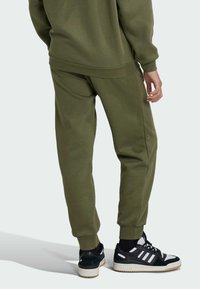 Maslinasto zelene trenirke s rebrastim manžetama i pojasom, izrađene od mekog materijala. Crno-bijele tenisice s teksturiranim dovršetkom i bijelim potplatom.