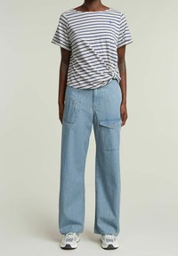 Camiseta de algodón a rayas con un frente anudado, combinada con pantalones cargos de mezclilla ligera azul claro, sueltos y con bolsillos.