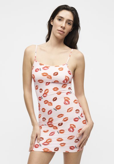 Γυναίκα που φοράει ένα λευκό εφαρμοστό φόρεμα με λεπτές τιράντες, με πολύχρωμο μοτίβο κόκκινων και πορτοκαλί χειλιών.