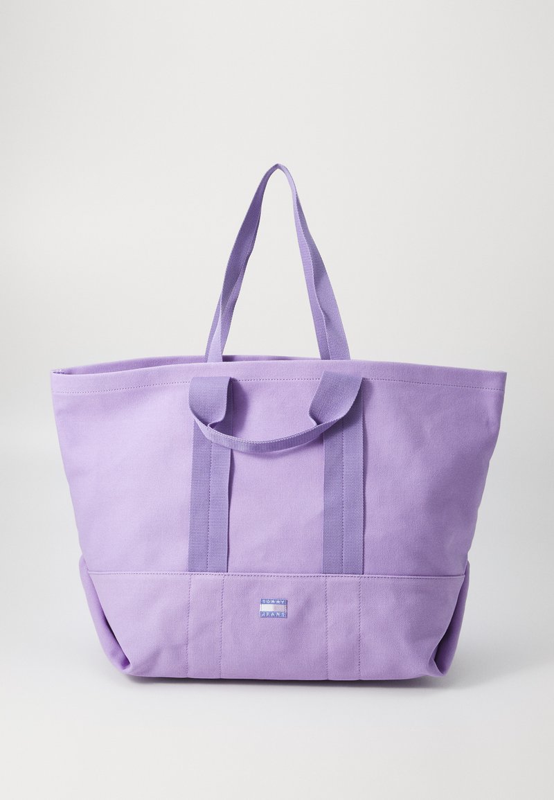 Borsa tote in tela viola con due manici superiori, uno spazioso scomparto principale e una base rettangolare. Presenta una piccola etichetta con logo sulla parte anteriore.
